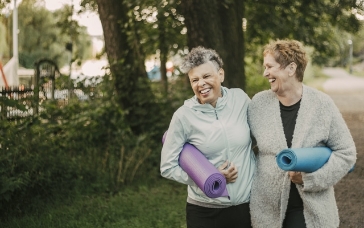 Two women smiling holding yoga mats